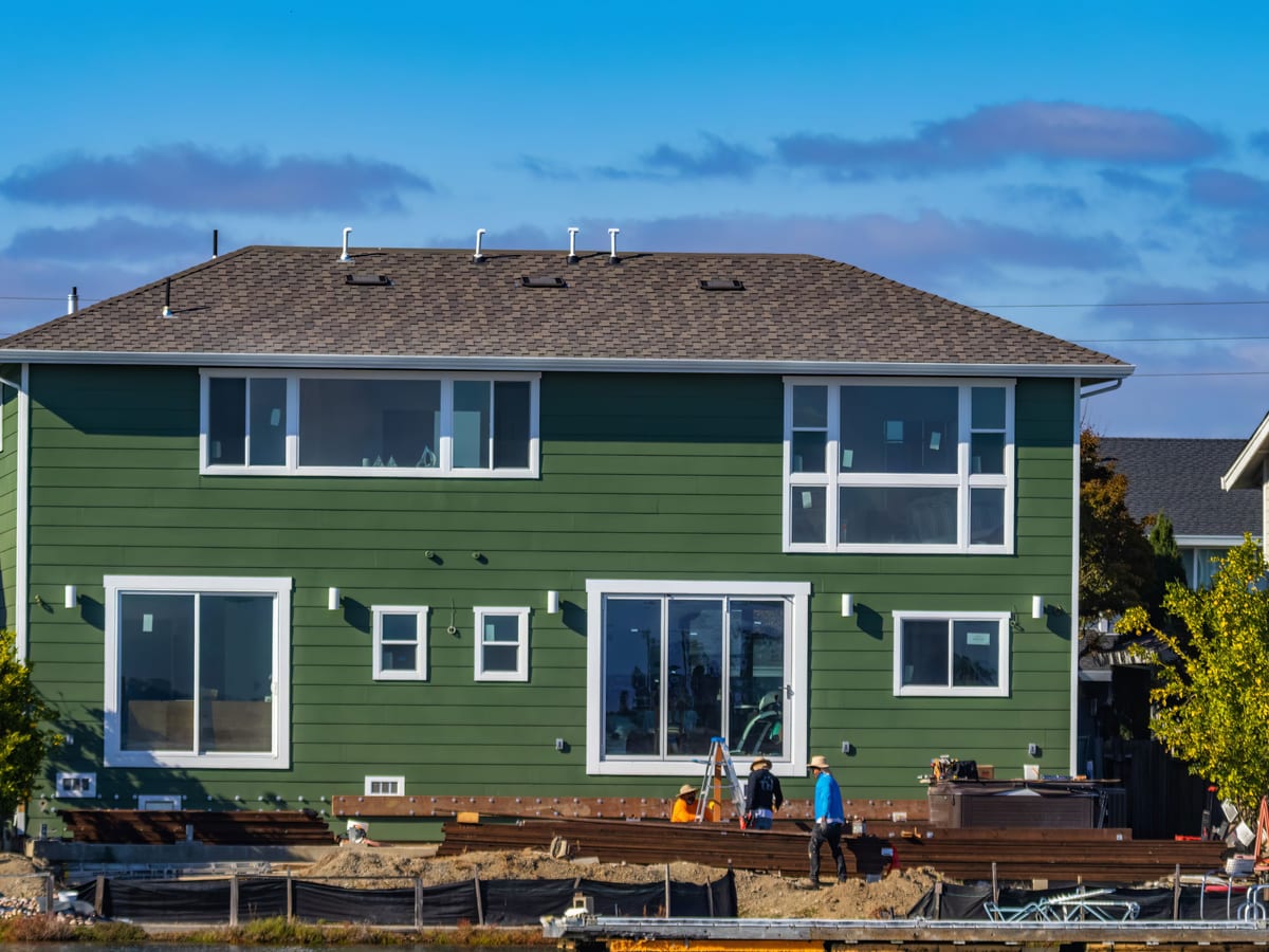 A modern green house under construction with blue skies and workers outside.